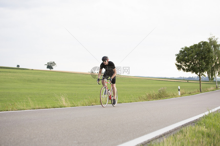 沿乡村公路骑自行车的成年男子图片