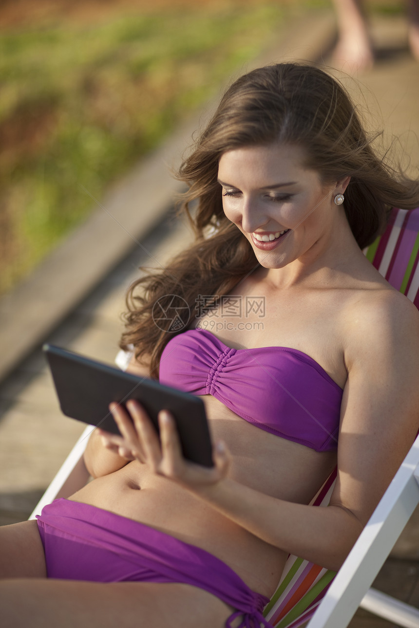 坐在沙滩椅子上看数字平板电脑的年轻女士图片