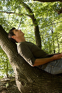 成年男性靠在树林里的树干上休息图片