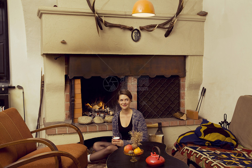 坐在壁炉旁边地板上的年轻妇女肖像图片