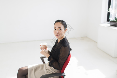 坐在有咖啡的办公椅上年轻妇女图片