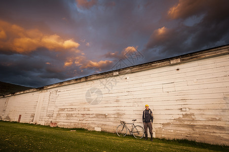 年轻人站在白墙旁边骑着自行车背景图片