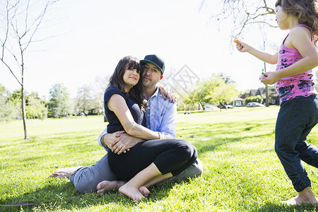 绑腿与年轻女儿一起坐在公园的成年中夫妇背景
