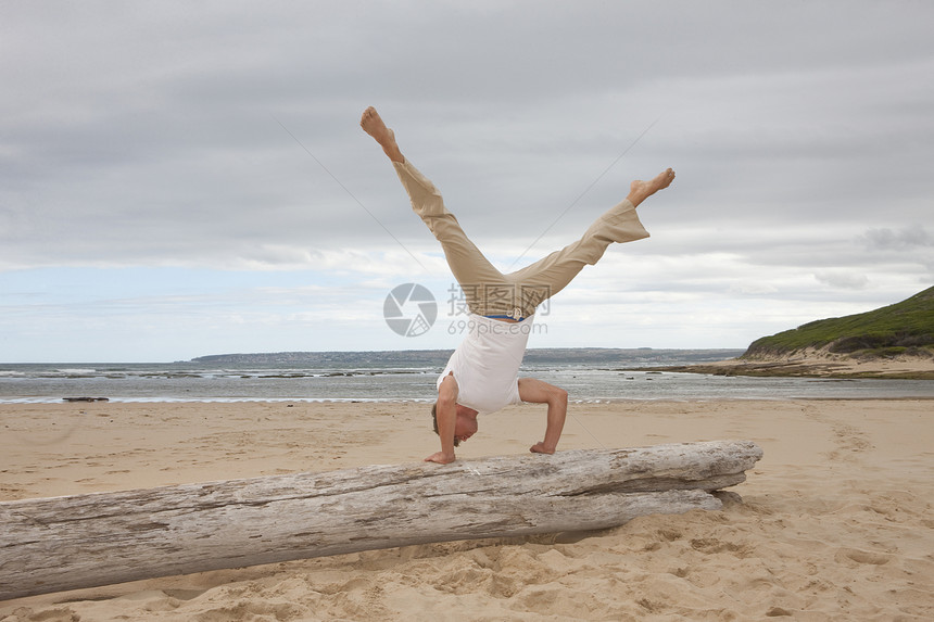 年轻男子在海滩上撑着树干做倒立运动图片