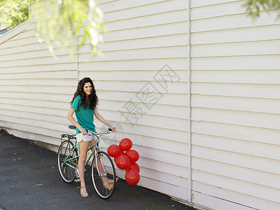 年轻女性坐在带一堆气球的自行车上图片