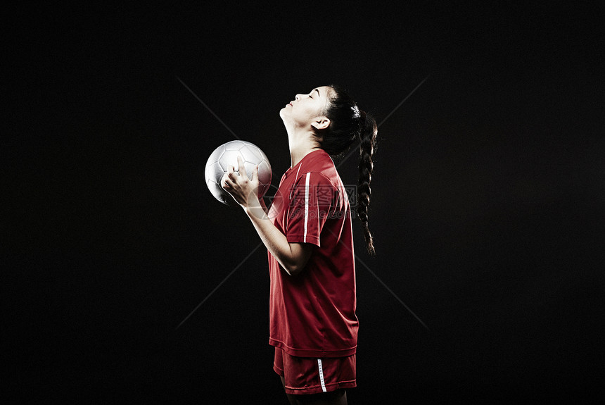 黑色背景下年轻女子拿着足球抬头图片