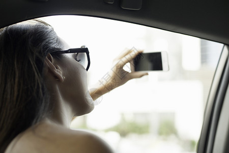 年轻女子在出租车窗口用智能手机拍照图片