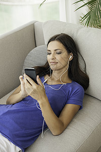 女青年靠在沙发上听智能手机音乐图片