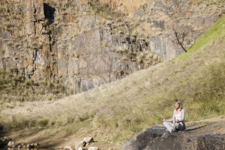 在湖边岩石做瑜伽的年轻女子图片