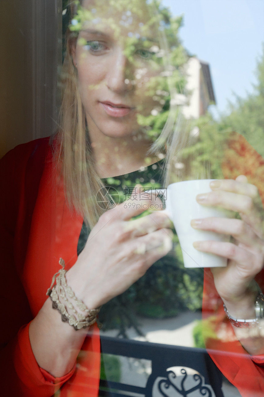 端着咖啡杯望向窗外的年轻女人图片