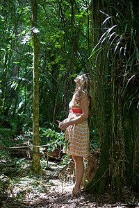 年轻女子靠在丛林中的树上朝上看图片