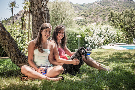 在家庭花园草地上坐着两个女性朋友和宠物狗肖像图片