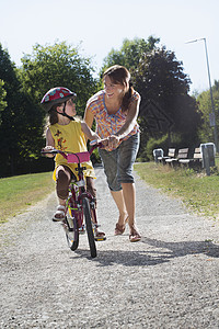 年轻女孩与母亲一起学习骑自行车图片