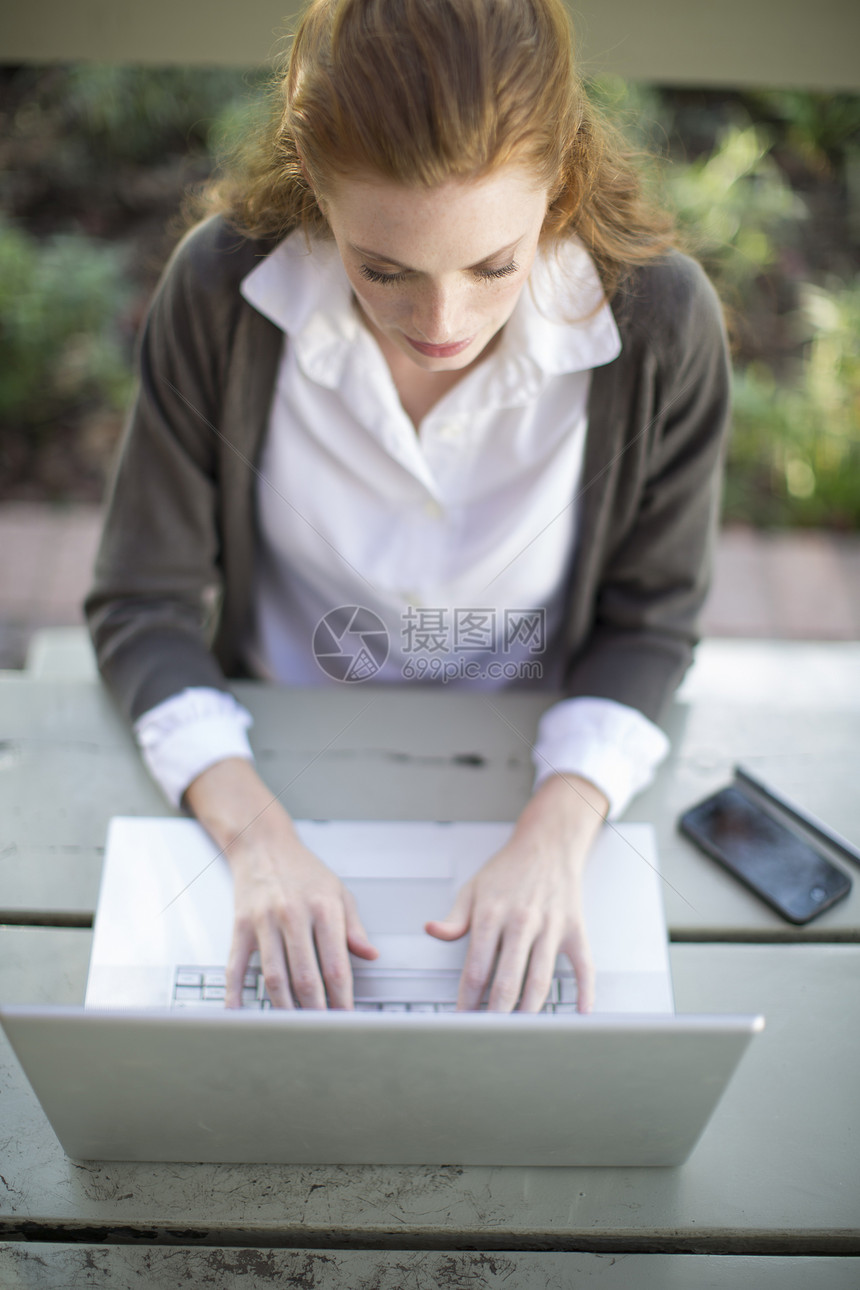 青年女商人在花园桌上的笔记本电脑上打字图片