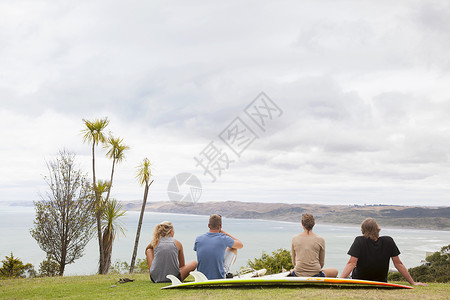 坐在草地上观海的四名青年人图片