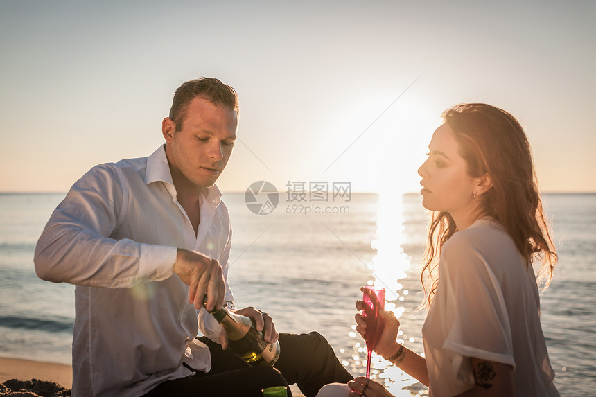 在海滩上喝香槟的年轻夫妇图片