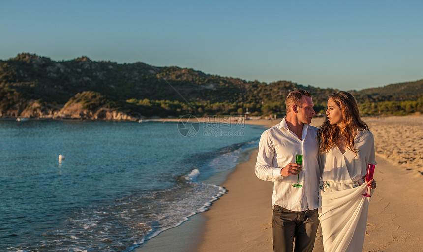 在海滩上带着香槟漫步的年轻夫妇图片