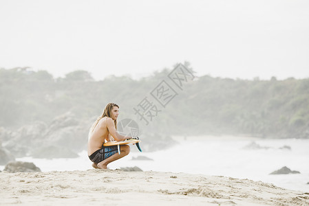 坐在海边拿着冲浪板的男人图片