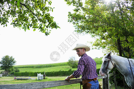 穿牛仔装的年轻男子骑马检查栅栏图片