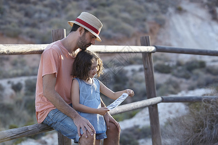 父亲和女儿坐在栅栏上读纸条图片