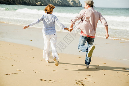 在海滩上手牵手奔跑的成熟夫妇高清图片