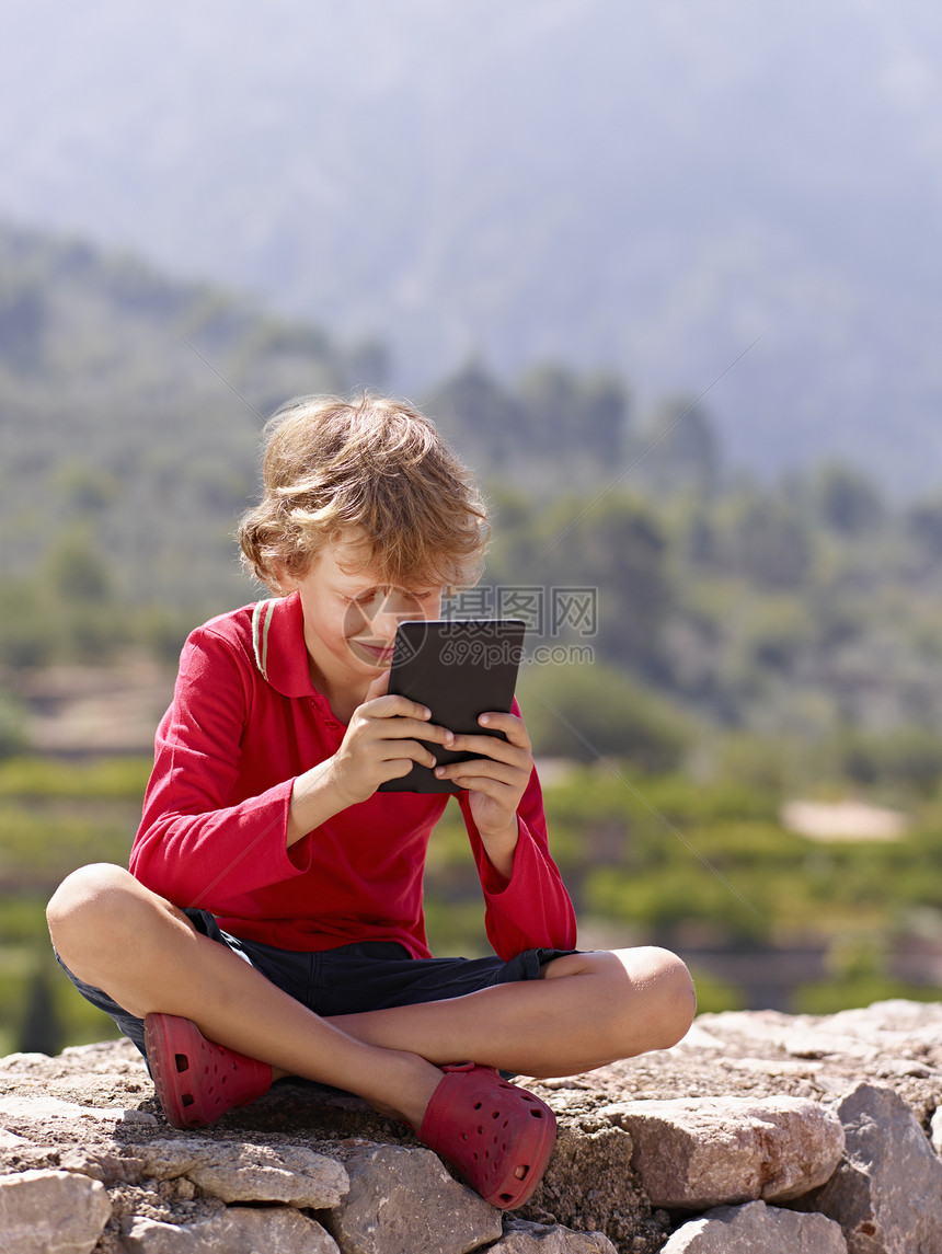 坐在石墙上看着数字石板的男孩西班牙马杰卡图片