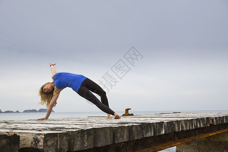 做瑜伽的中年成女子在木制海滨码头移动图片