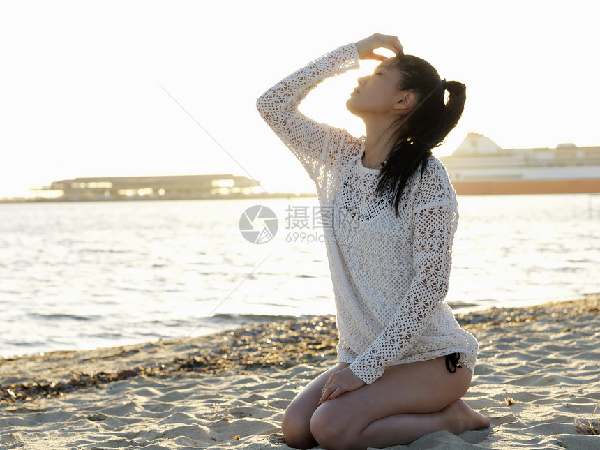 澳大利亚维多利亚州墨尔本港年轻女子跪在阳光明媚的海滩上图片