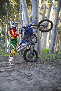 年轻男运动员骑摩托车站在森林轨道上图片