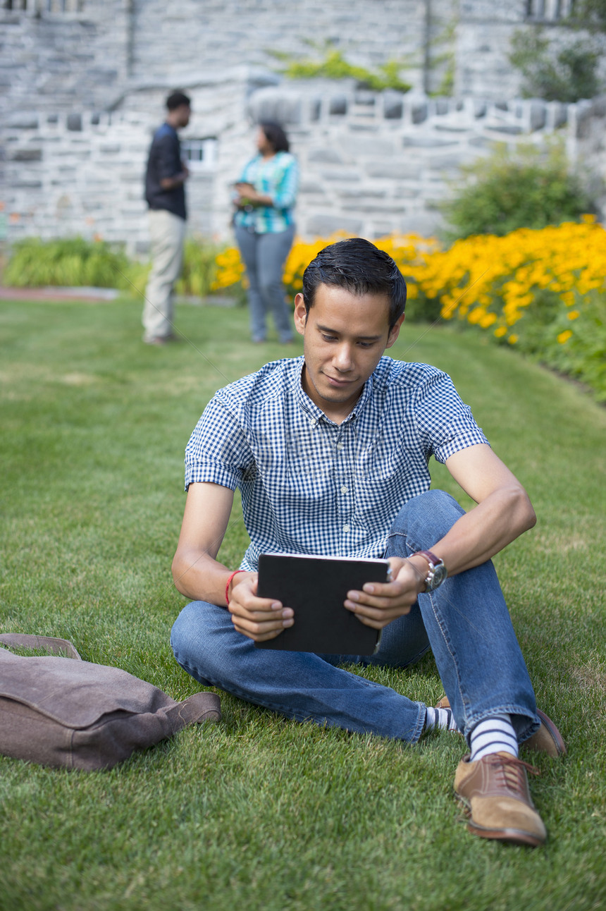坐在草地上使用平板电脑的男学生图片