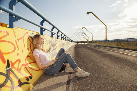 沐浴着阳光坐在涂鸦桥上的年轻女士图片
