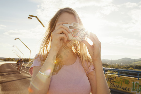 在桥上用数码相机拍照的年轻女子图片
