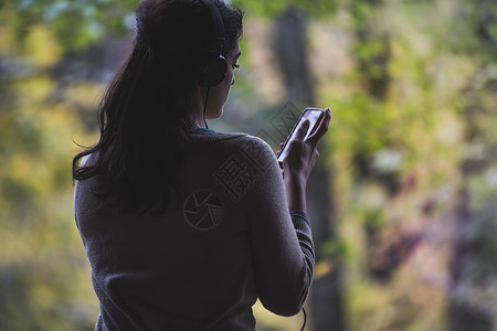 公园中的年轻女子戴耳机听歌玩手机图片