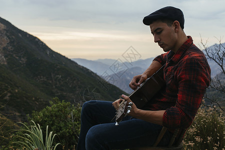 坐在山地的年轻人弹着吉他图片