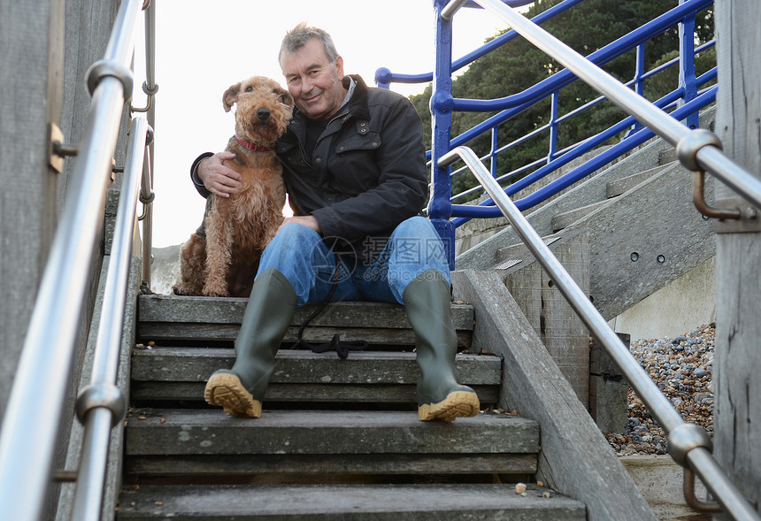 抱着狗狗坐在台阶上的年长男子图片