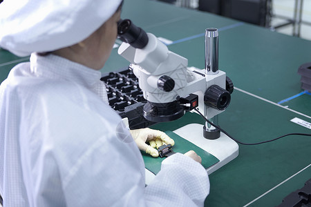 在工厂中使用显微镜的工人该厂专门在灵活表面上创建功能电路图片