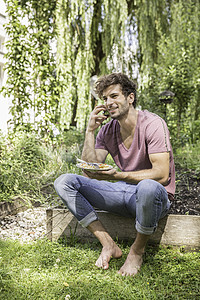 在花园的年轻人用手机和食物盘子的手机在花园里图片