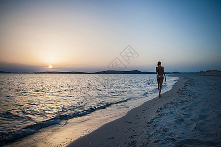 年轻女子穿着比基尼漫步在海滩上图片