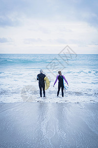 父亲和女儿拿着冲浪板一起踏入大海图片