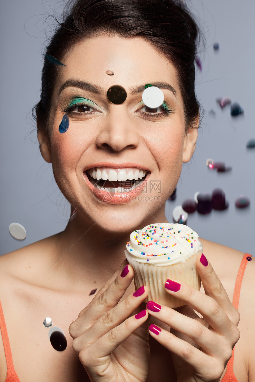 拿着纸杯蛋糕脸上沾着亮片微笑的女人图片