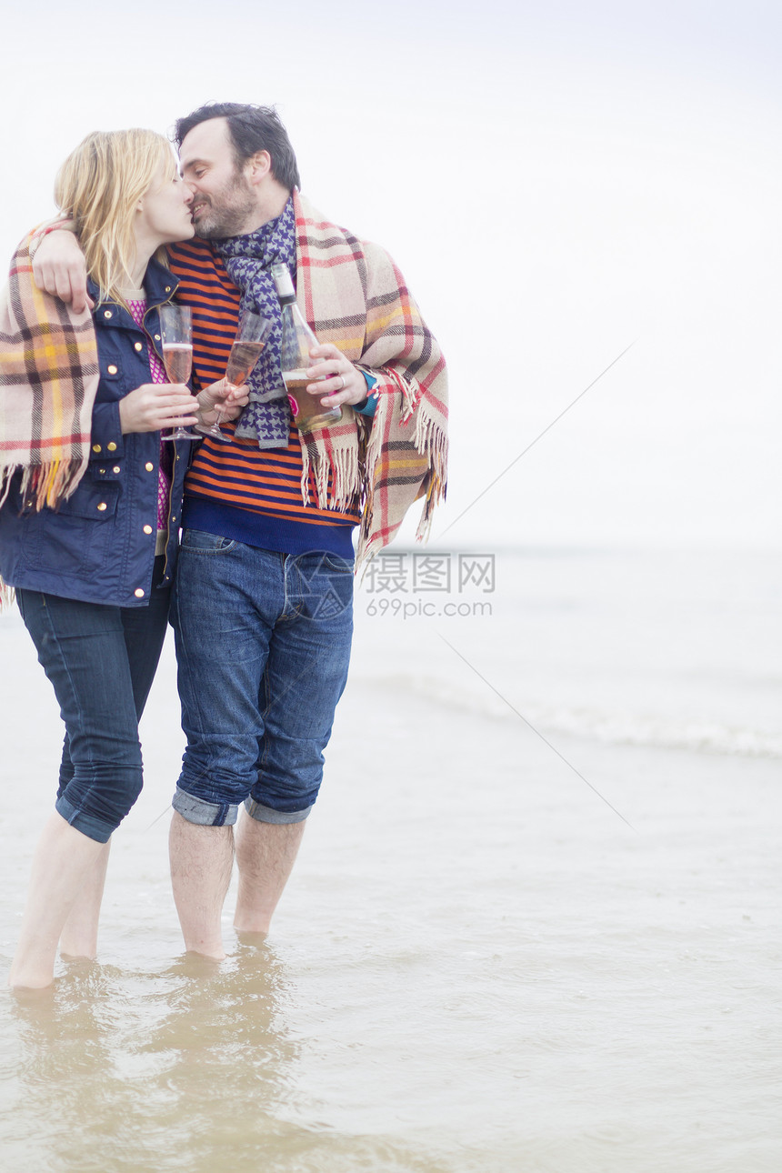 夫妇握着葡萄酒在海中行走亲吻图片
