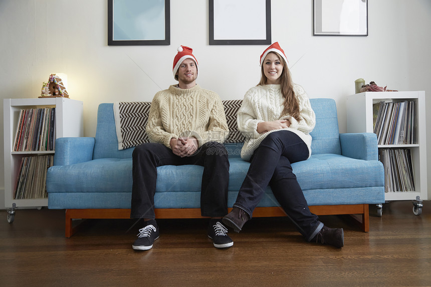 坐在客厅沙发上戴着圣诞帽的年轻夫妇图片