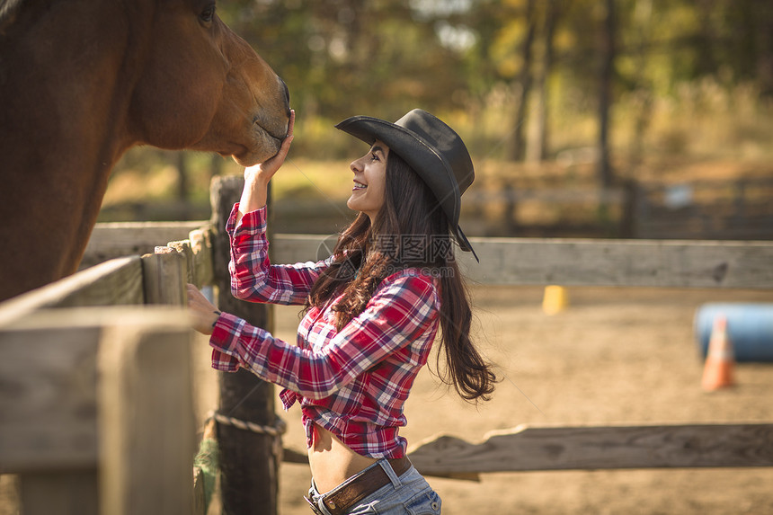 牛仔女孩在牧场上抚摸马图片