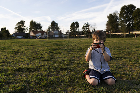 男孩在公园里跪看着数码相机图片
