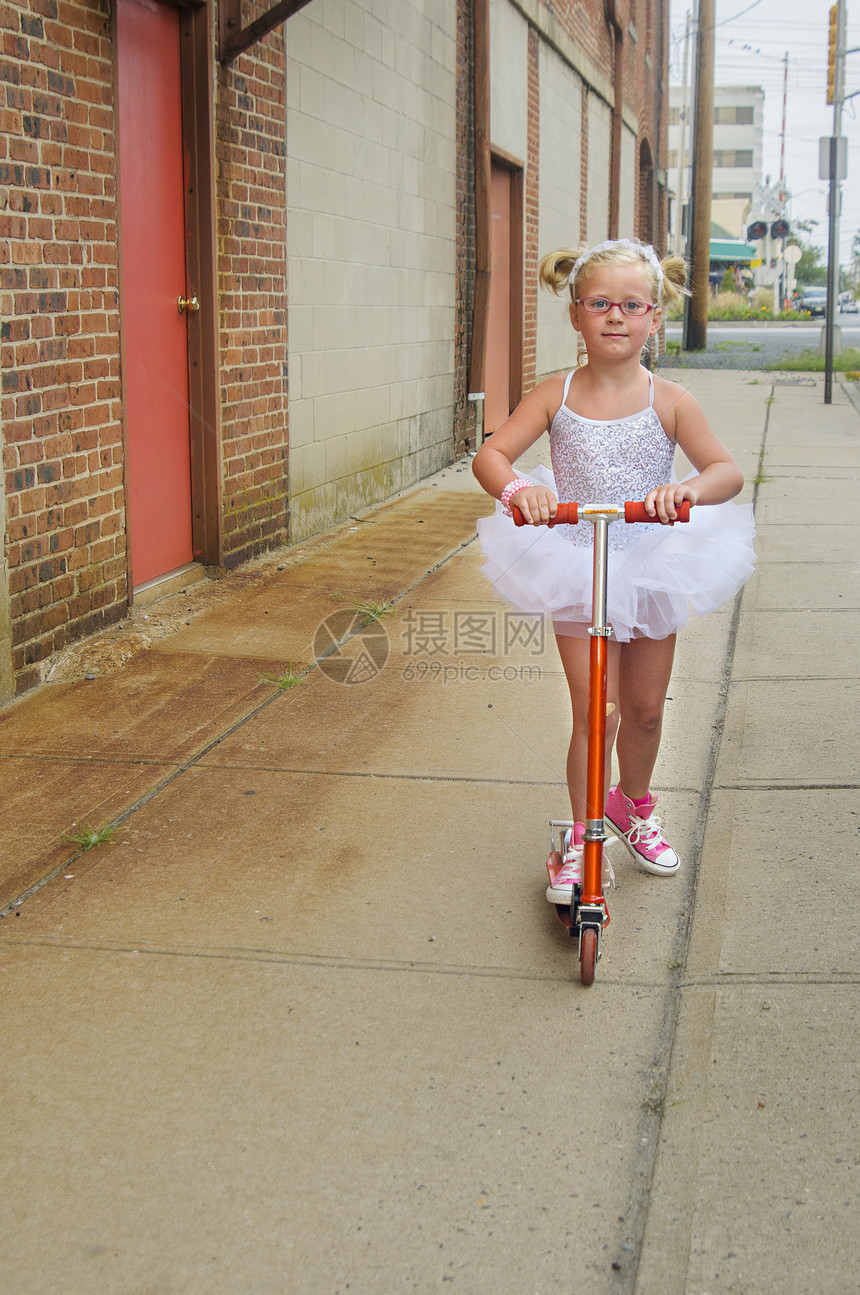 女孩穿着芭蕾舞裙和粉红色棒球靴玩滑板车图片
