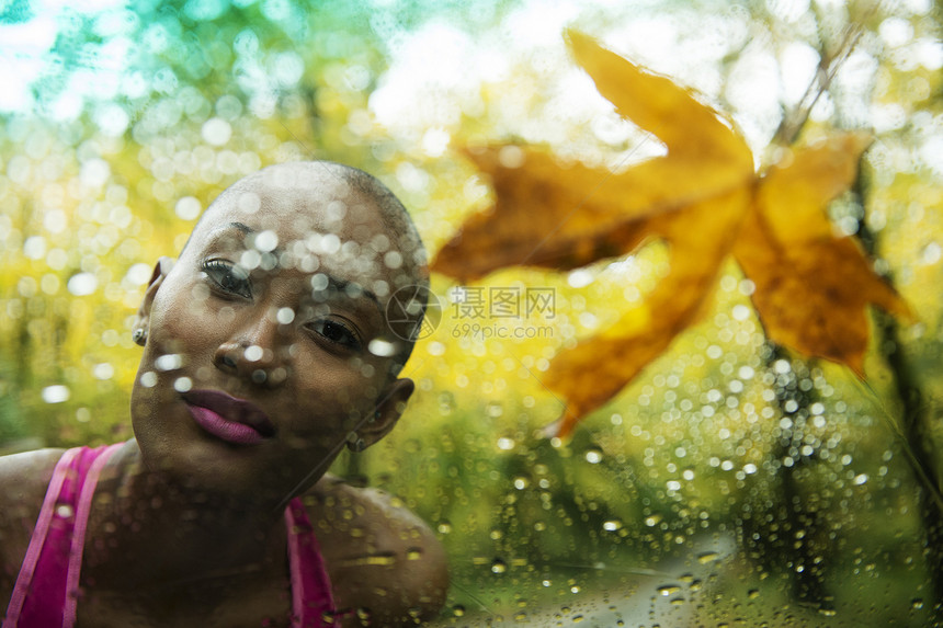 透过被雨水打湿的窗户玻璃看到的年轻女子的肖像图片