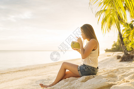 海滩上喝新鲜椰子汁的年轻女性图片