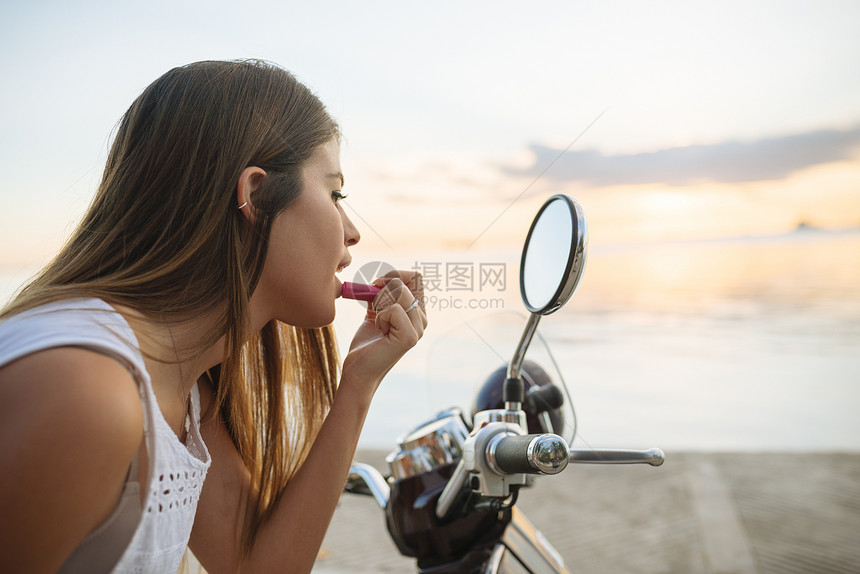 在摩托车镜子上涂口红的年轻女性图片