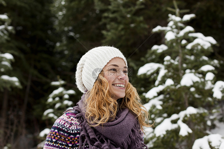 微笑的年轻女人站在雪覆盖的树前的肖像图片