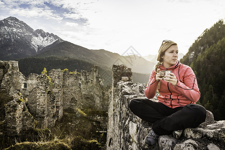 在奥地利蒂罗尔州的城堡废墟旁边喝咖啡的年轻女子高清图片